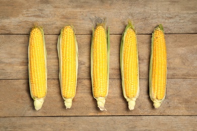 Photo of Tasty sweet corn cobs on wooden table, flat lay