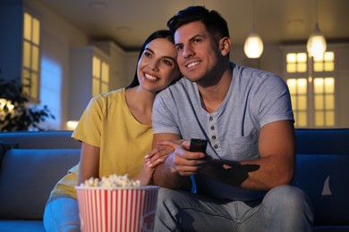 Couple watching movie with popcorn on sofa at night