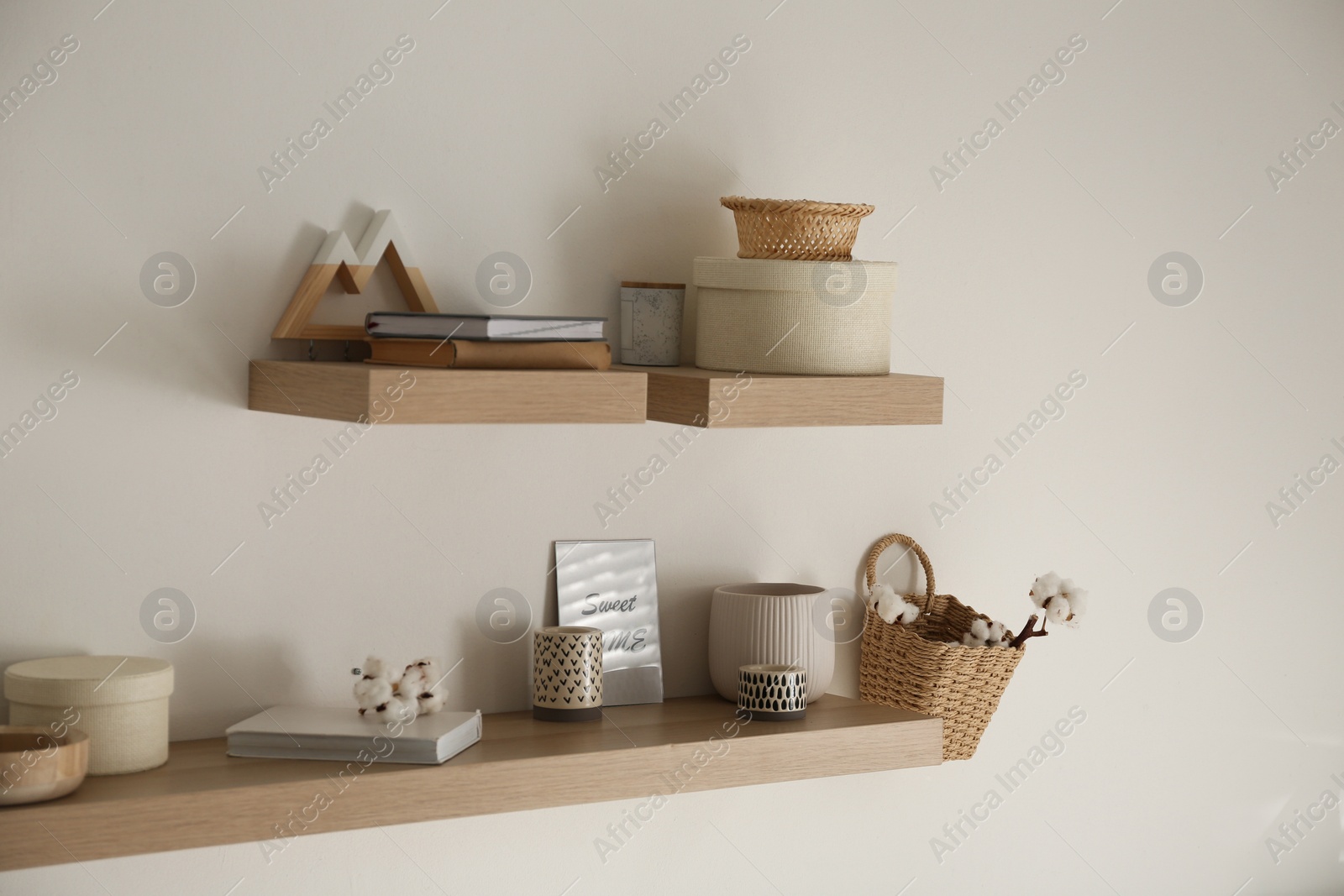 Photo of Wooden shelves with books and different decorative elements on light wall