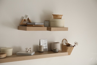 Photo of Wooden shelves with books and different decorative elements on light wall