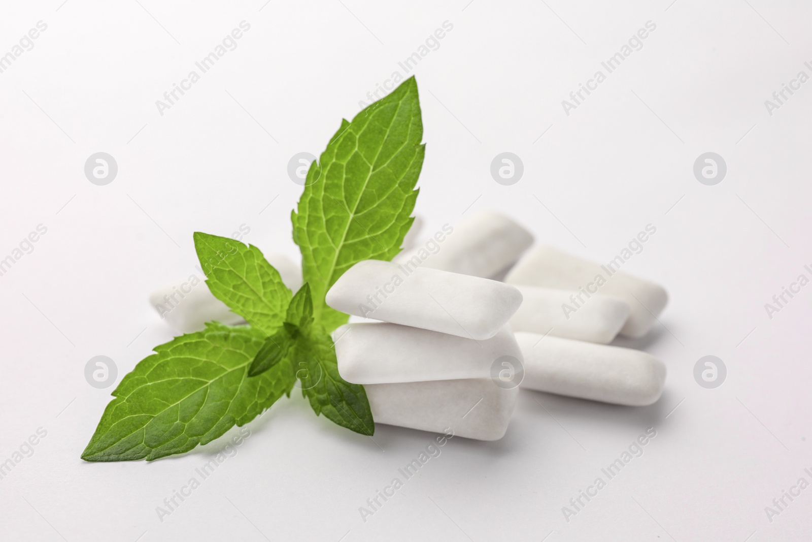 Photo of Tasty chewing gums and mint leaves on white background, closeup