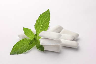 Photo of Tasty chewing gums and mint leaves on white background, closeup