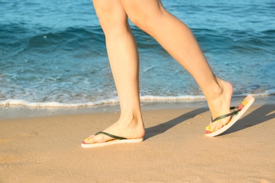 Photo of Closeup of woman with flip flops on sand near sea. Beach accessories