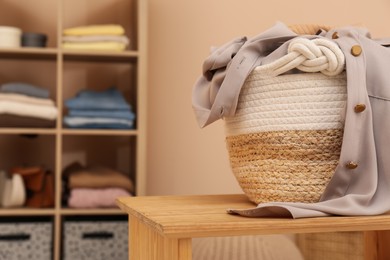 Wicker laundry basket overfilled with clothes on wooden table indoors. Space for text