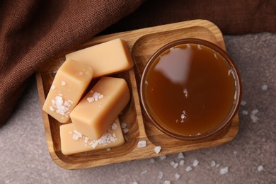 Photo of Yummy caramel candies, sauce and sea salt on brown table, top view