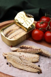 Photo of Delicious canned mackerel fillets and fresh tomatoes on wooden board, closeup