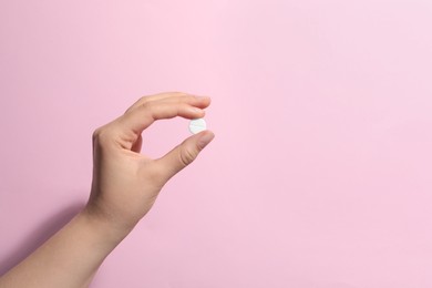 Woman holding pill on pink background, closeup. Space for text