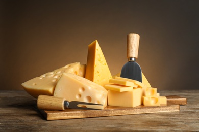 Photo of Different sorts of cheese, fork and knife on wooden table