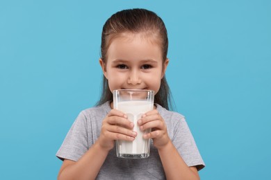 Cute girl with glass of fresh milk on light blue background