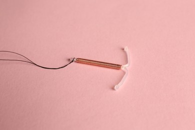Photo of T-shaped intrauterine birth control device on pink background