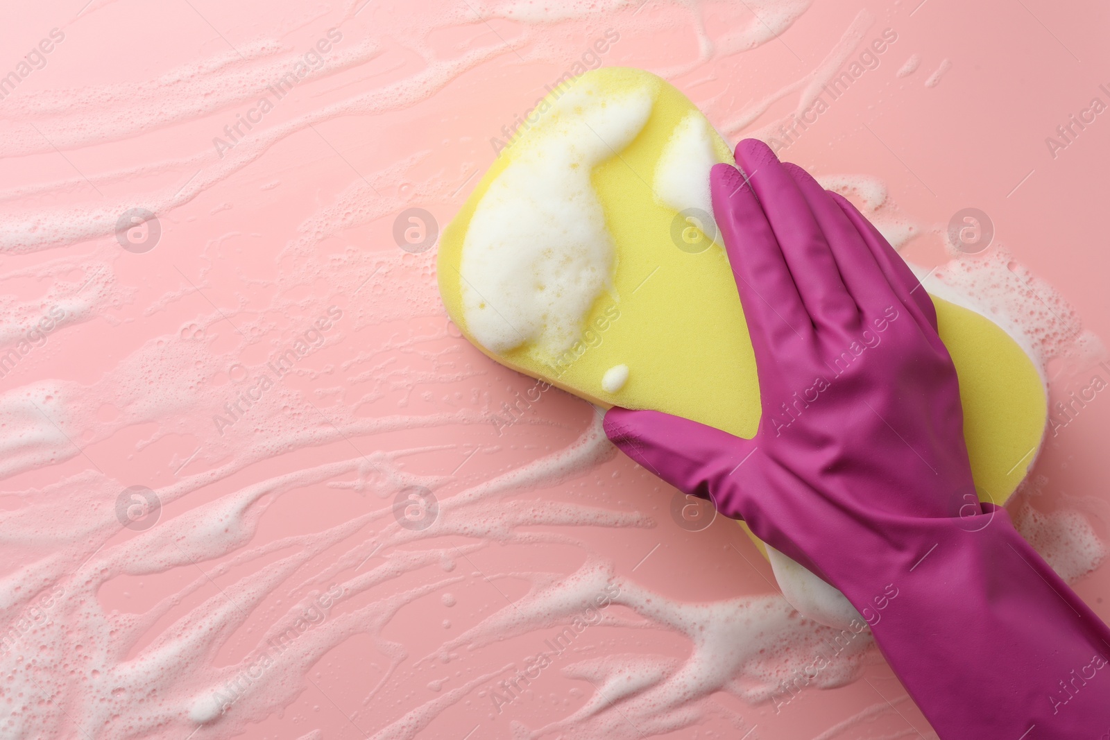 Photo of Cleaner in rubber glove holding sponge with foam on pink background, top view.