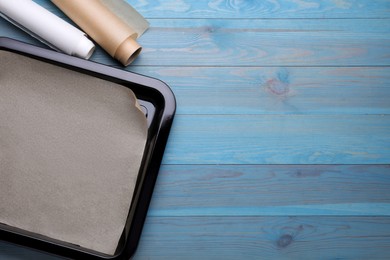 Photo of Rolls of parchment paper and baking pan on light blue wooden table, flat lay. Space for text