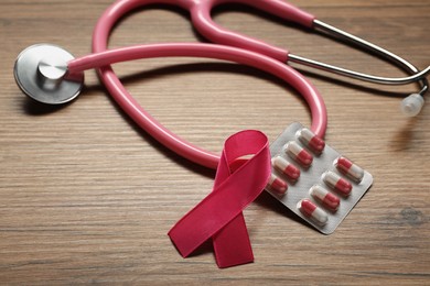 Photo of Pink ribbon, stethoscope and pills on wooden table. Breast cancer awareness