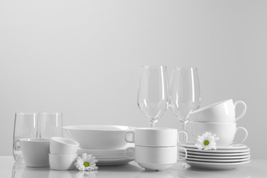 Photo of Set of many clean dishware, flowers and glasses on light table. Space for text