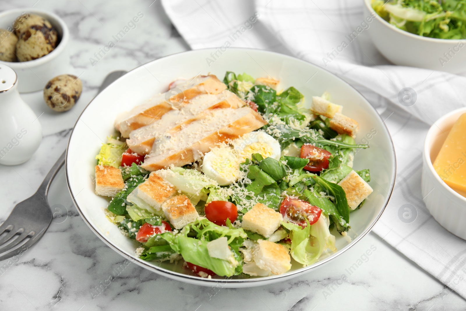 Photo of Delicious Caesar salad in bowl on white marble table