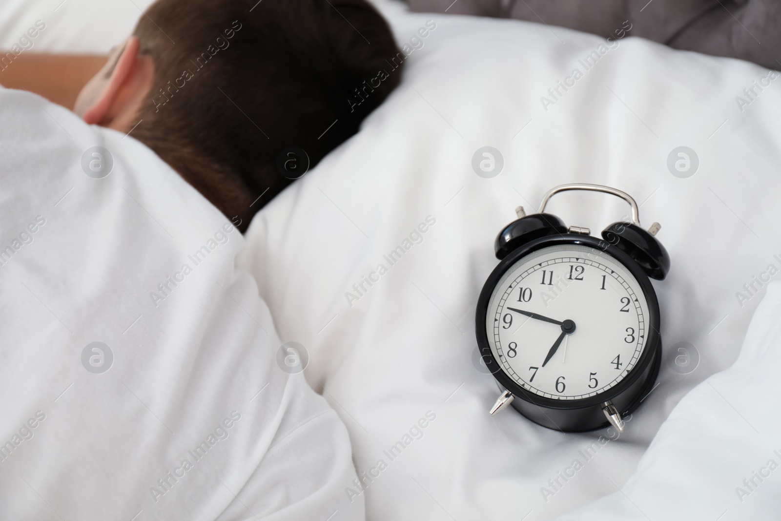 Photo of Analog alarm clock and sleepy man in bed. Time of day