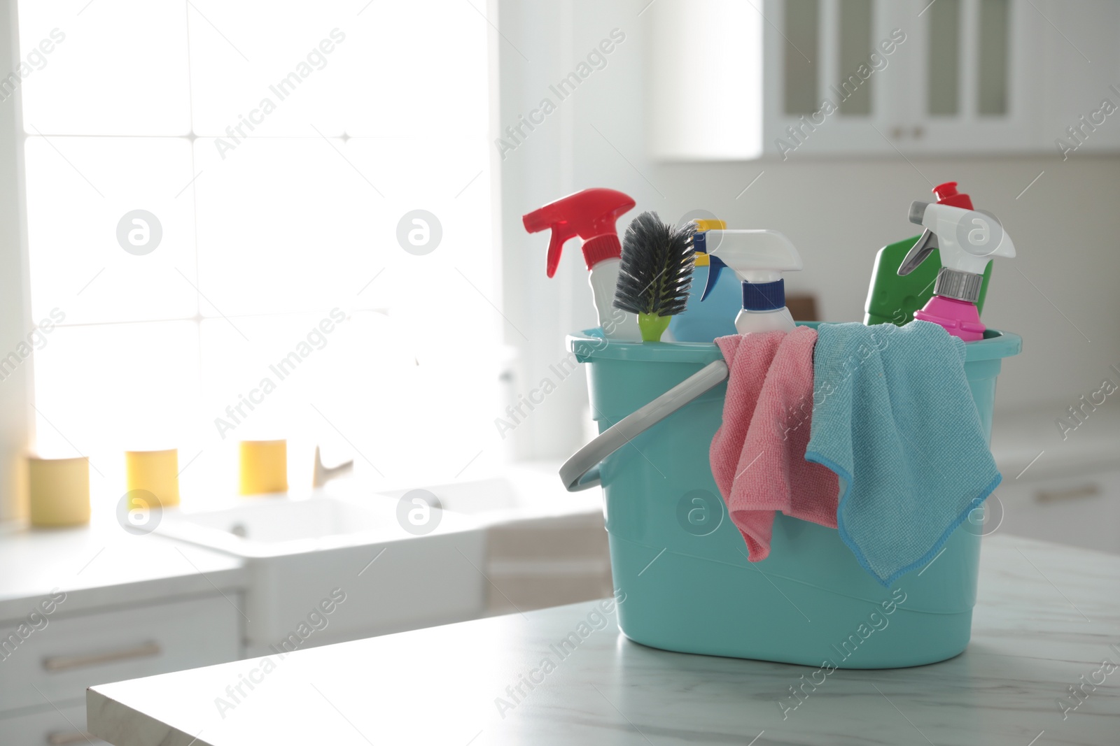 Photo of Plastic bucket with different cleaning supplies on table in kitchen. Space for text