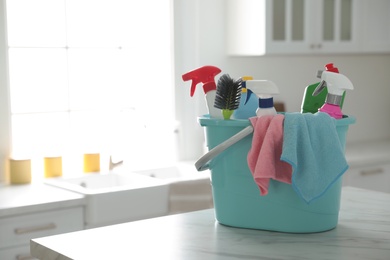 Plastic bucket with different cleaning supplies on table in kitchen. Space for text