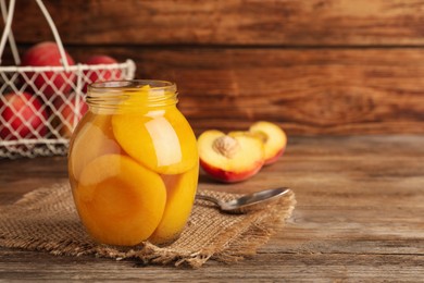 Canned peach halves in glass jar on wooden table, space for text