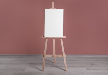 Photo of Wooden easel with blank canvas near dusty rose wall