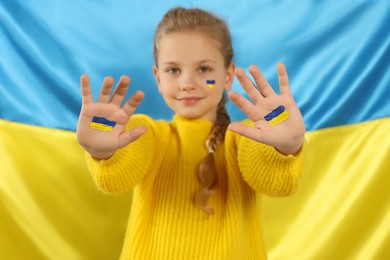 Photo of Little girl with paint on hands and face near Ukrainian flag