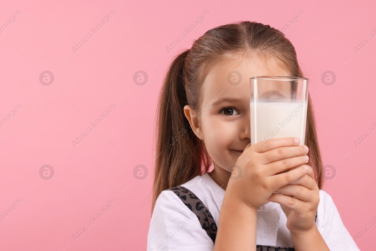 Photo of Cute girl with glass of fresh milk on pink background, space for text