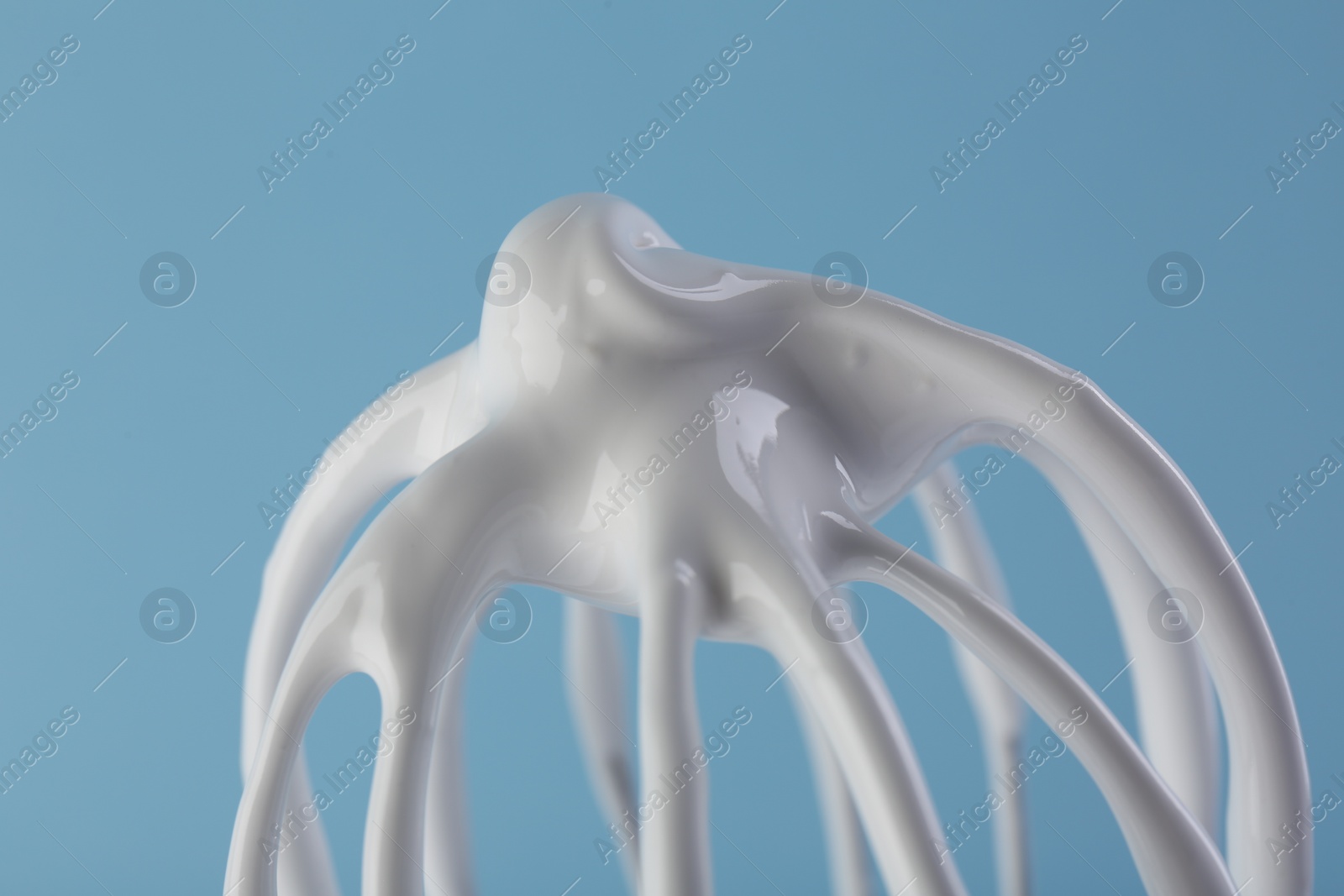 Photo of Whisk with whipped cream on light blue background, closeup