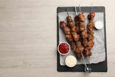 Metal skewers with delicious meat, ketchup and sauce served on white wooden table, top view. Space for text