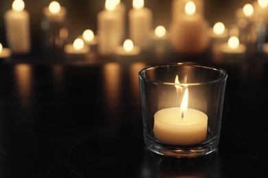 Burning candle on table in darkness, space for text. Funeral symbol