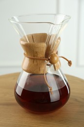 Photo of Glass chemex coffeemaker with coffee on wooden table, closeup