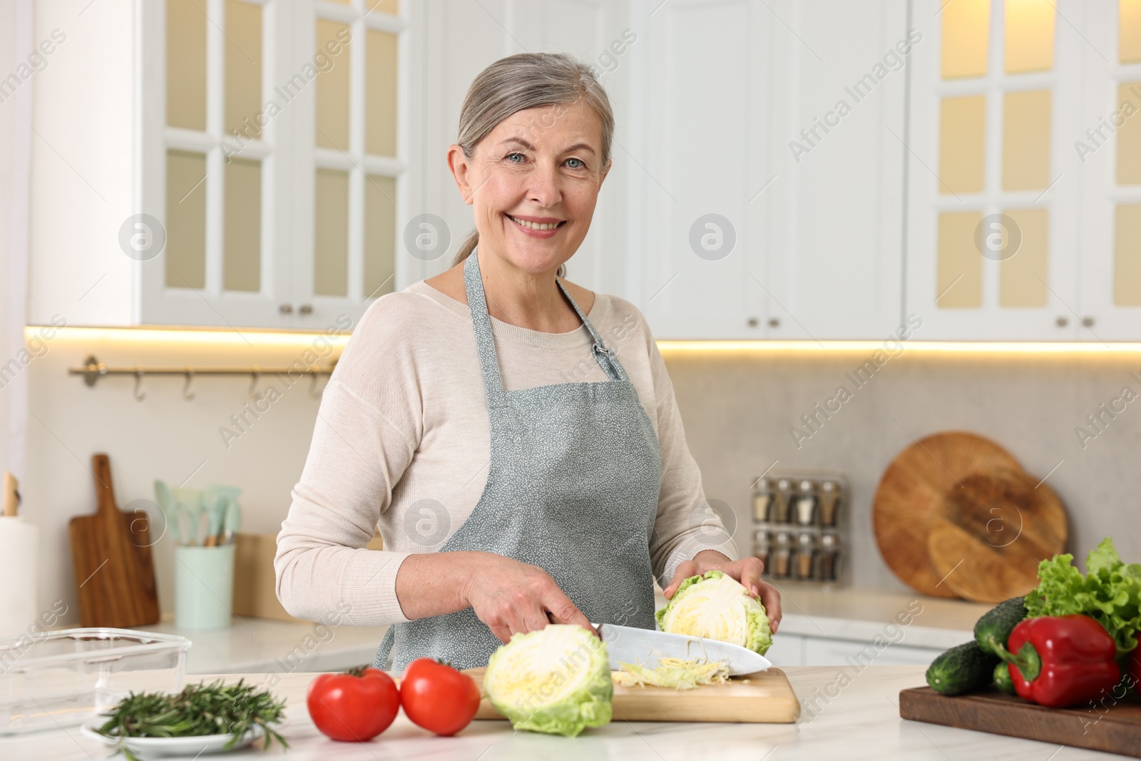 Photo of Happy housewife cutting cabbage at table in kitchen