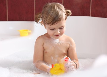 Photo of Little girl bathing with toy ducks in tub