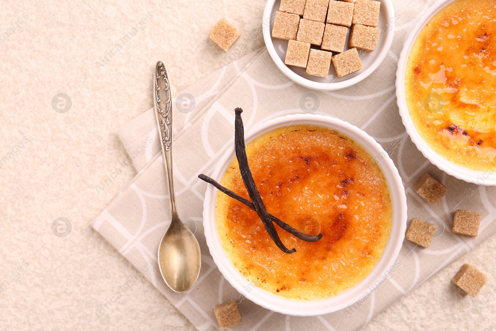 Photo of Delicious creme brulee in bowls, vanilla pods, sugar cubes and spoon on light textured table, top view