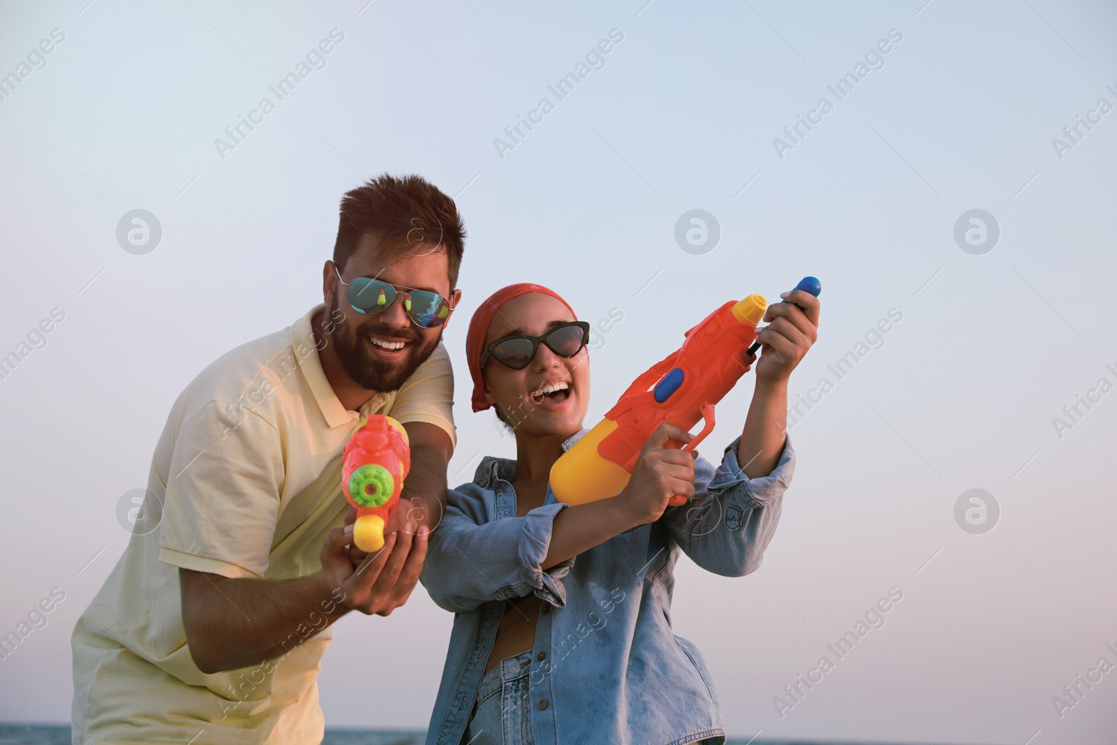 Photo of Happy couple with water guns against light blue sky at sunset