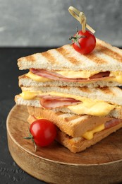 Stack of tasty sandwiches with ham and melted cheese served with tomatoes on black textured table, closeup