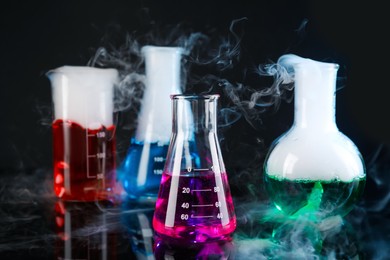 Photo of Laboratory glassware with colorful liquids and steam on black background. Chemical reaction