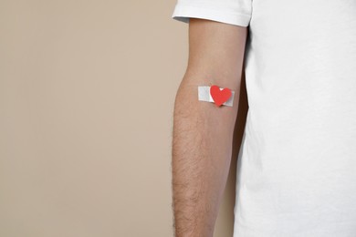 Photo of Blood donation concept. Man with adhesive plaster on arm against beige background, closeup. Space for text
