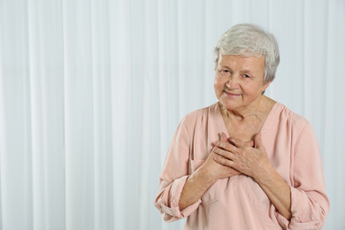 Photo of Grateful senior woman with hands on chest against light background. Space for text