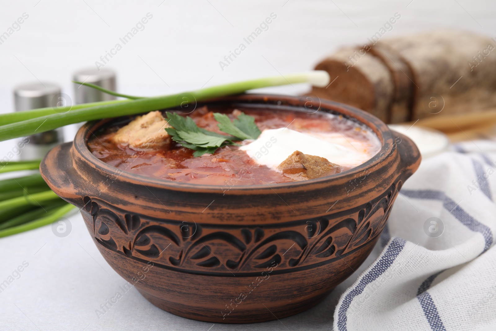 Photo of Tasty borscht with sour cream in bowl served with green onion on light grey table, closeup