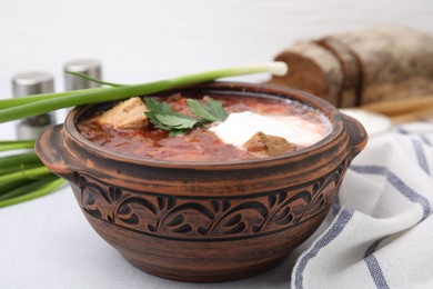 Photo of Tasty borscht with sour cream in bowl served with green onion on light grey table, closeup