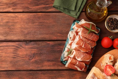 Photo of Rolled slices of delicious jamon and different products on wooden table, flat lay. Space for text