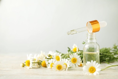 Bottle of chamomile essential oil and flowers on white table, space for text