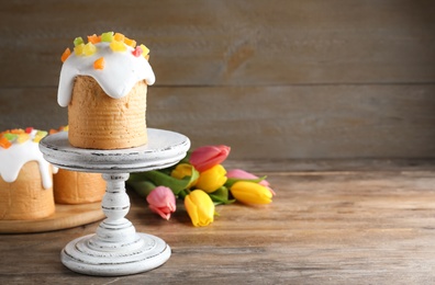 Photo of Stand with traditional Easter cake and beautiful tulips on wooden table. Space for text