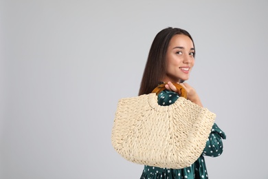 Young woman with stylish straw bag on light grey background. Space for text