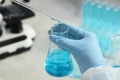 Scientist dripping liquid from pipette into beaker in laboratory, closeup