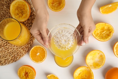 Photo of Woman pouring freshly made orange juice in glass at white table, top view