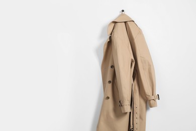Photo of Beige trench coat hanging on hook rack on white wall, space for text