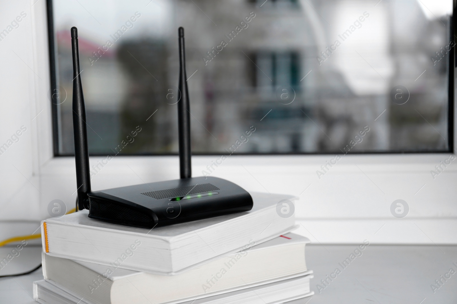 Photo of Modern Wi-Fi router on stack of books near window indoors. Space for text