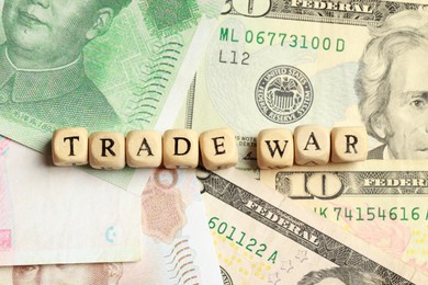 Photo of Wooden cubes with phrase Trade war on different banknotes, flat lay