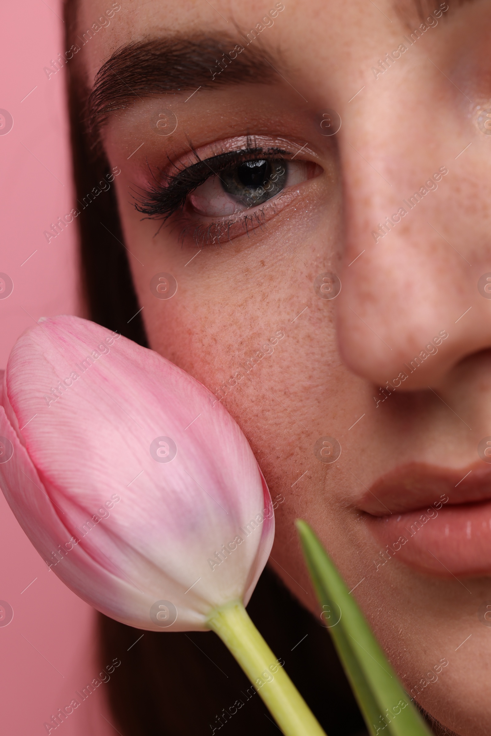 Photo of Beautiful woman with freckles and tulip on pink background, closeup